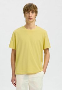 T-shirt à manches courtes, col rond, en doux coton jaune, présentant une coupe décontractée et un ourlet droit. Design uni sans motifs.