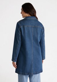 Jachetă din denim de culoare albastru închis, cu un guler, mâneci lungi și o tăietură dreaptă. Cusuturi vizibile și lungime până la mijlocul coapselor.