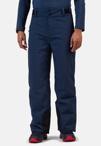 Pantaloni da neve impermeabili blu navy con vestibilità rilassata, dotati di due tasche anteriori con zip e dettagli neri sulla parte inferiore delle gambe.