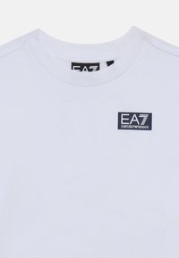 Biela bavlnená tričko s okrúhlym výstrihom a krátkymi rukávmi, s malým námorníkovým logom "EA7 Emporio Armani" na prednej strane.