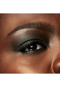 Close-up van een oog met donkere smokey eyeshadow, gedefinieerde wimpers en een verzorgde wenkbrauw op een zachte, warmgetinte huid als achtergrond.