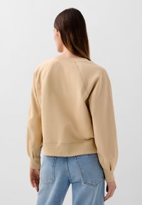 Beiger, übergroßer Sweatshirt mit gerippten Bündchen und Saum. Verfügt über Ballonärmel und eine einfache, glatte Textur. Getragen mit hellblauen Jeans.
