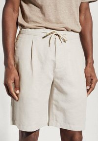 Shorts en lin beige avec une coupe décontractée, dotés d'une taille à cordon, de poches latérales et de plis subtils pour plus de détails.