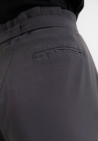 Szare spodnie wykonane z gładkiego materiału, z szerokim pasem i tylną kieszenią. Projekt jest nowoczesny, z czystymi liniami i minimalnymi detalami.