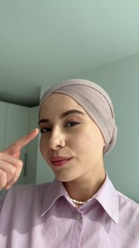 Ljusrosa huvudduk i texturerat tyg, bärs tillsammans med en randig rosa skjorta. Personen har en ansiktspiercing och en neutral bakgrund.