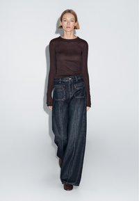 Brown long-sleeve top paired with high-waisted, wide-leg dark denim jeans featuring front and back pockets, and contrasting stitching details.