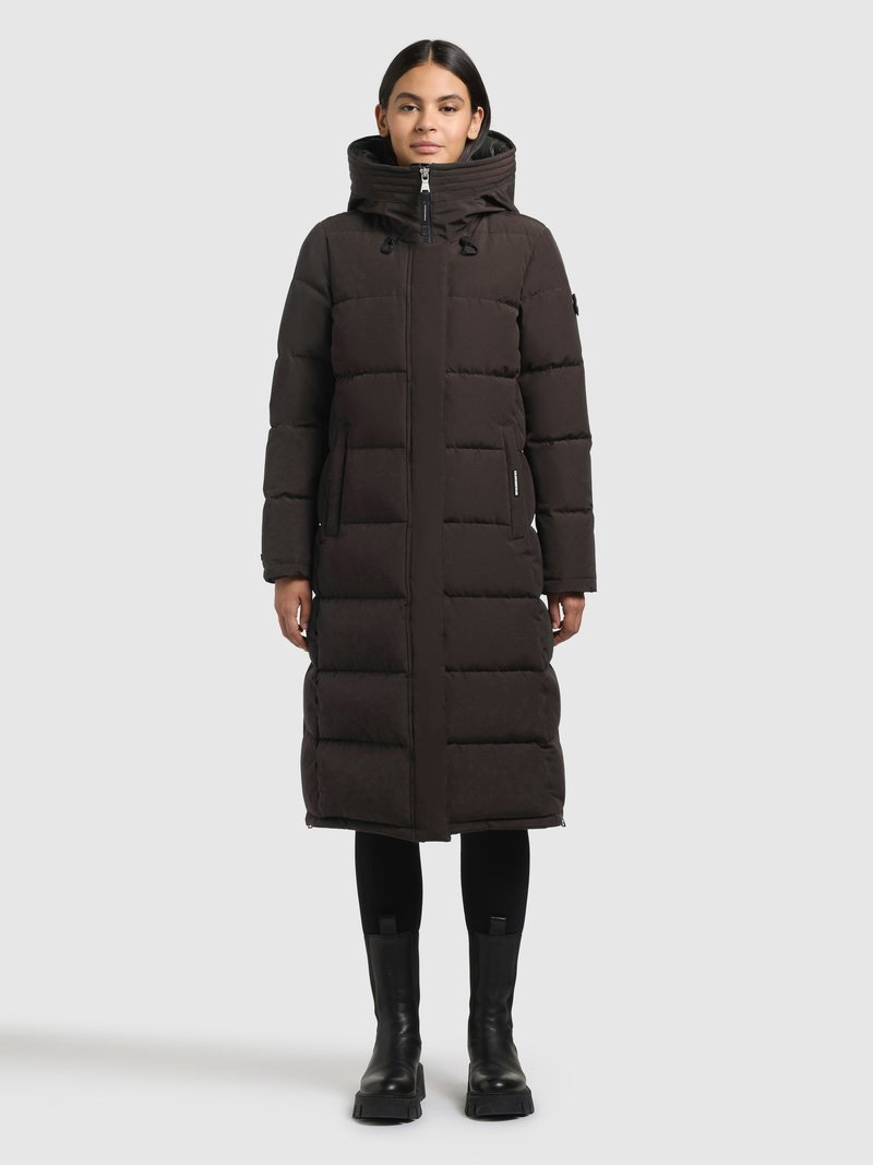 Pikk must sulejope kõrge krae ja kapuutsiga, millel on esilukk, küljetaskud ja tikitud muster. Kandmiseks valitud mustad retuusid ja saapad.