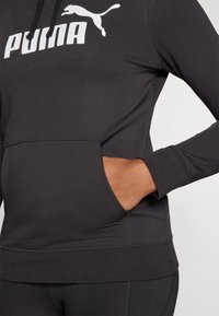 Felpa nera con cappuccio e un grande logo bianco "PUMA" sul petto, dotata di tasca frontale e polsini a coste per una vestibilità comoda.