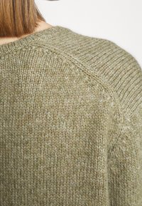 Pull en maille avec un col rond et des manches raglan, présentant un tissu doux et texturé dans une couleur vert olive discret.