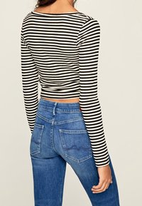 Svart- och vitrandig långärmad topp som matchas med blå högmidjade jeans med fickor och en synlig sömdetalj på baksidan.