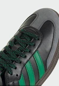 Black and gray leather sneaker with green stripes. Features textured black laces with green speckles and a rubber sole.