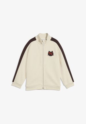 Cremefarbene Zip-Up-Jacke mit schwarzen Streifen an den Ärmeln und einem kleinen schwarzen Katzenkopf-Logo mit rotem Design auf der linken Brust.