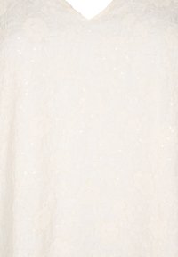 Blouse en dentelle avec un décolleté en V, en blanc cassé, ornée de motifs floraux et de sequins pour plus de texture et de détails.