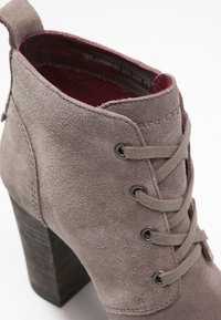 Gray suede ankle boot with a textured finish, featuring a chunky wooden heel, lace-up design, and a burgundy interior lining.