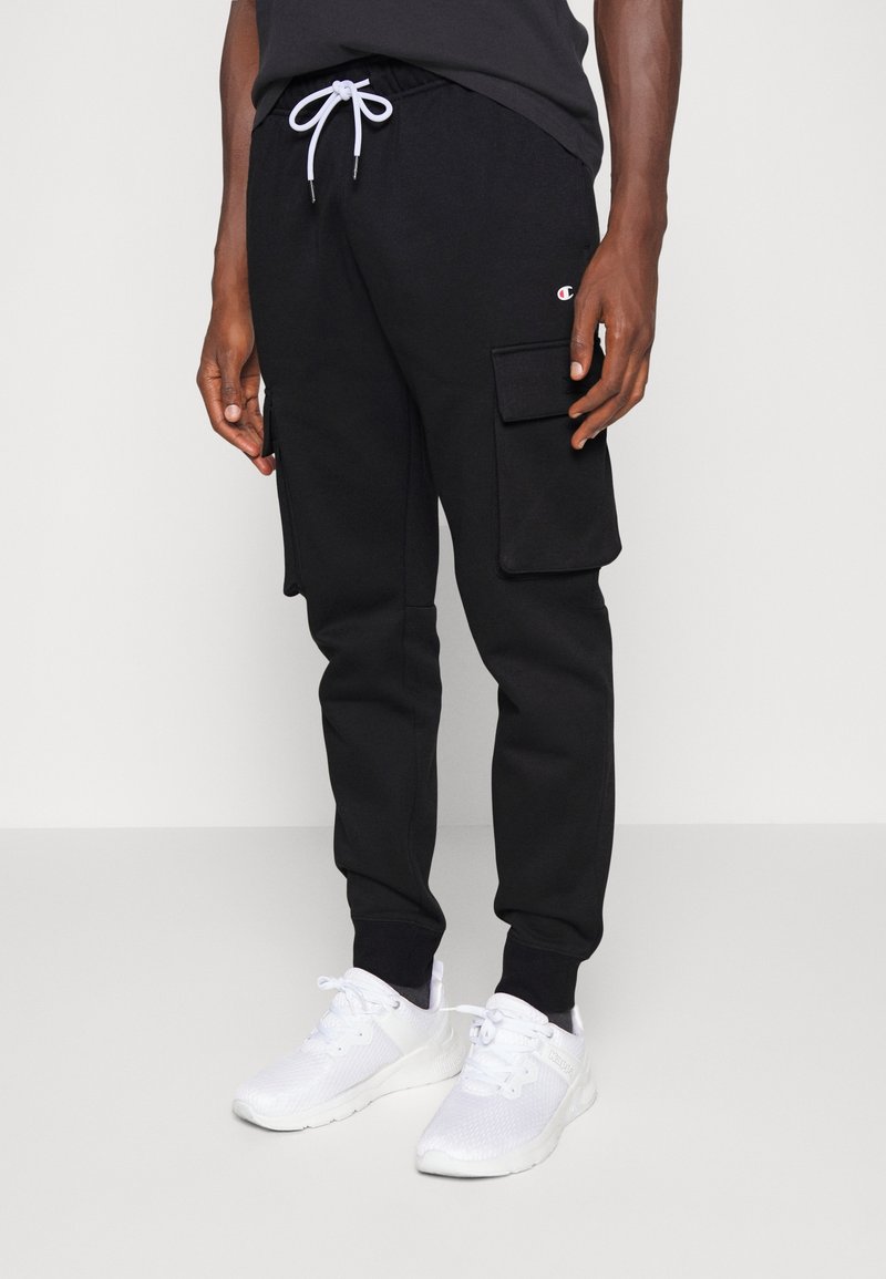 Svarta sweatpants med dragsko i midjan, sidofickor i cargo-stil och ribbad mudd. Bärs med vita sportskor.