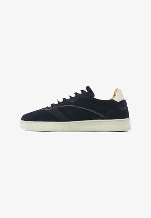 Navy suede sneaker with white laces and sole, beige heel tab, and zigzag stitching on the side.