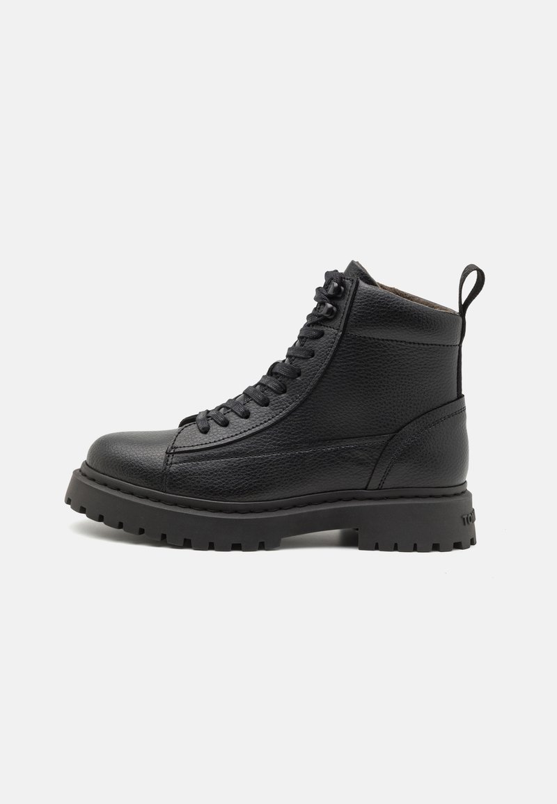 Botte montante en cuir noir avec semelle épaisse à crampons et fermeture à lacets à l'avant, équipée d'une languette à l'arrière pour un enfilage facile.