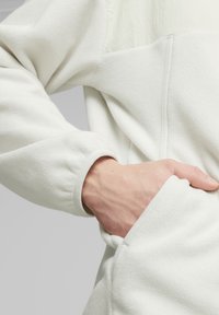 Pullover bianco in pile con un corpo texturizzato, tessuto morbido e una mano in una tasca laterale, con un orlo a contrasto.