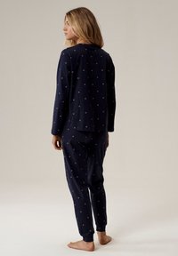 Granatowy zestaw piżamowy z miękkiego materiału, z okrągłym dekoltem, długimi rękawami i wzorem w kropki. Dopasowane mankiety w spodniach, luźny krój.