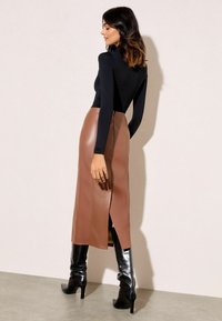 Melna garām piedurknēm topa kombinācija ar brūnu ādas midi svārku ar šķēlumu, papildināta ar melnām augstpapēžu zābakiem līdz augšstilbiem.