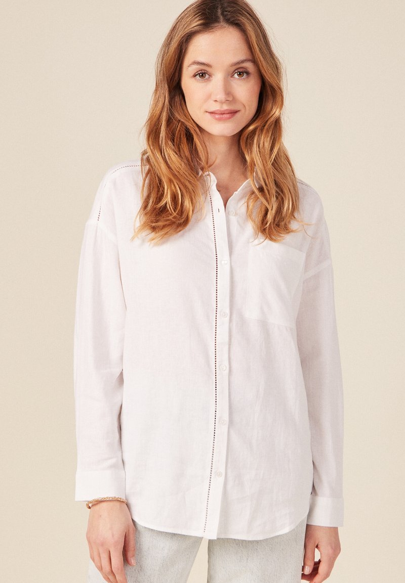 Camisa blanca de botones hecha de tejido ligero, con un bolsillo, un sutil detalle de costura a lo largo de la tapeta de los botones y mangas largas.