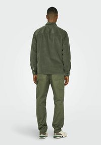 Veste chemise en velours côtelé vert olive avec col et poignets à boutons, associée à un pantalon cargo assorti doté de plusieurs poches.