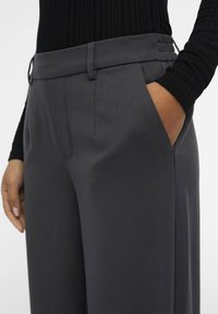 Grey tailored pants with a smooth texture, featuring side pockets and a crisp waistband. The fabric appears lightweight and durable.