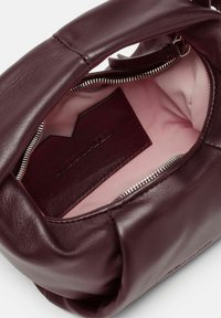 Interno di una borsa in pelle bordeaux con fodera rosa chiaro, zip argentata e un portacarte scuro decorato con dettagli del logo.