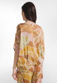 Luftig, brun bluse med farverige bladmønstre i pink og grøn, med en afslappet pasform og korte flagermusærmer.