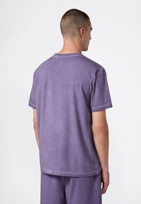 Fioletowy T-shirt z krótkim rękawem wykonany z miękkiego, strukturalnego materiału o luźnym kroju, z detalami przeszyć i okrągłym dekoltem.