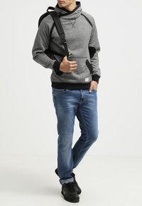 Sudadera con capucha en tonos gris y negro, con un alto cuello, bolsillo frontal y mangas raglán, combinada con unos vaqueros azules y zapatillas negras.