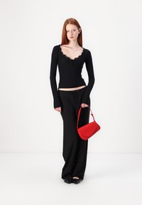 Black long-sleeve top with lace trim, paired with black wide-leg pants. Holding a small red handbag, wearing black shoes with decorative accents.