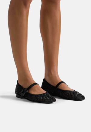 Bailarinas negras con punta afilada, que presentan un textura trenzada y una hebilla decorativa. Tacón bajo; correas en el empeine para mayor soporte.