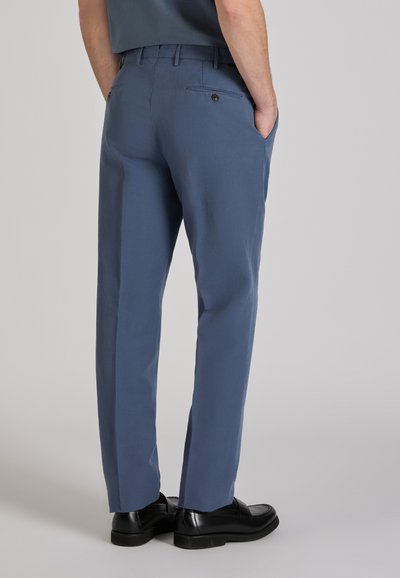 Blue, loose-fitting pants with a smooth texture, featuring two back pockets and a fitted waistband, paired with black loafers.