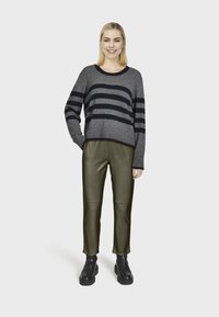 Pull en laine gris rayé de lignes marines, au design cropped ; associé à un pantalon en cuir synthétique vert olive et des bottines noires. Un style simple et moderne.