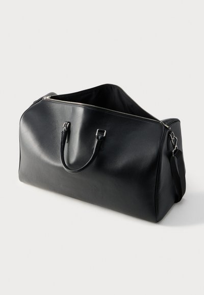 Borsa da viaggio in pelle nera con doppie maniglie e cerniera aperta, dotata di tracolla staccabile su sfondo bianco semplice.