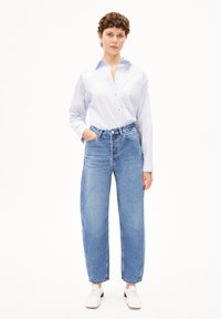 Hellblaues Hemd mit langen Ärmeln, kombiniert mit hochgeschnittenen, locker sitzenden blauen Jeans. Die Jeans haben einen ausgefransten Saum.