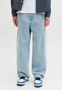 Világoskék, bő szabású, farmervászonból készült nadrág, magas derékrésszel és egyenes szárakkal. Fehér sportcipőkkel párosítva, melyeken kék és fekete részletek találhatók.