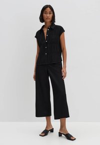 Camicetta nera a maniche corte con un motivo testurizzato, abbinata a pantaloni neri a gamba larga e mule neri con tacco a blocco.