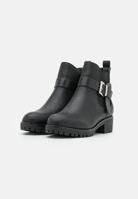 Bottines noires en cuir lisse avec une sangle texturée réglable et une boucle en argent, dotées d'une semelle épaisse pour plus de traction.