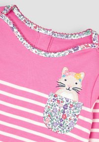 Roosa triibuline pika varrukaga topp, millel on kassi aplikaat taskul, lillemustriga tasku kangas ja volangiga kaeluse detail.
