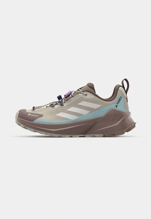 Beige and brown trail running shoes with textured fabric, white stripes, turquoise accents, and a rear pull tab; features quick-lace system.