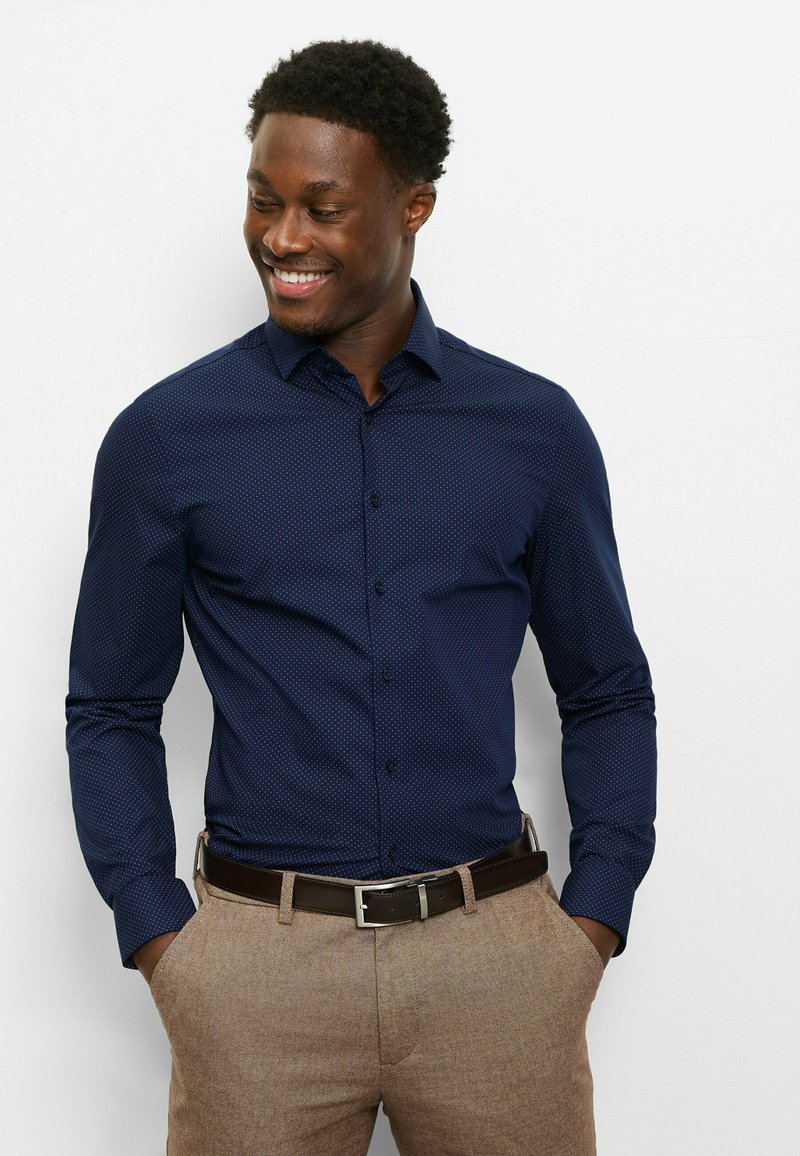 Navy blue button-up shirt with a subtle white polka dot pattern, paired with light brown textured pants and a brown belt.