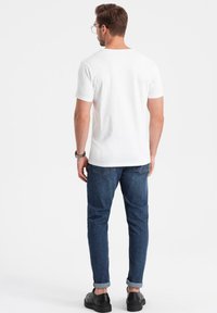 T-shirt bianca in cotone a maniche corte, abbinata a jeans blu scuro. I jeans sono arrotolati sui polsini e presentano tasche posteriori. Scarpe nere.