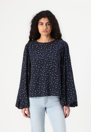 Blouse marine avec des manches longues et volumineuses et un décolleté festonné. Présente un motif floral avec des fleurs roses sur un fond sombre.