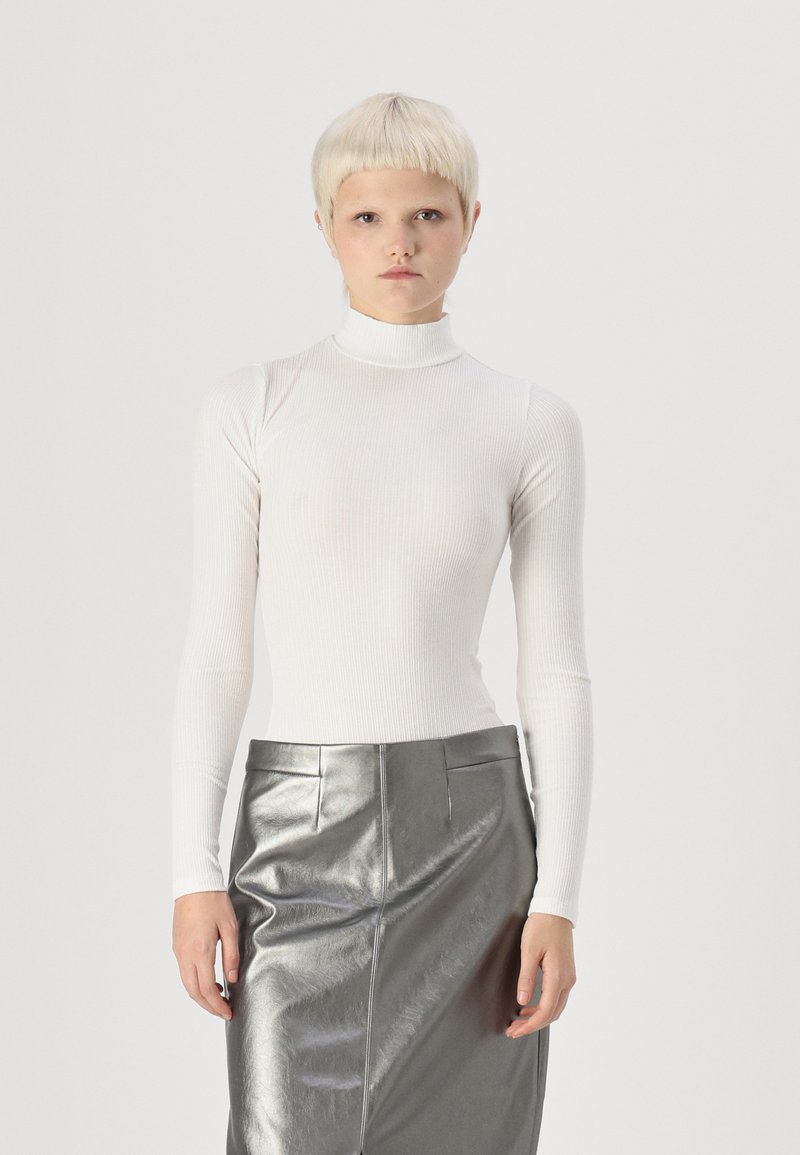 Hvit, ribbestrikket turtleneck med lange ermer, kombinert med et metallisk sølvfarget blyantskjørt som har en glatt tekstur og en tettsittende silhuett.