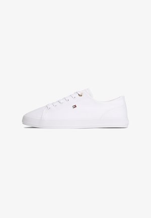 Witte lage sneaker met vetersluiting, klein rood-wit-zwart vlaglogo aan de zijkant en platte rubberen zool.