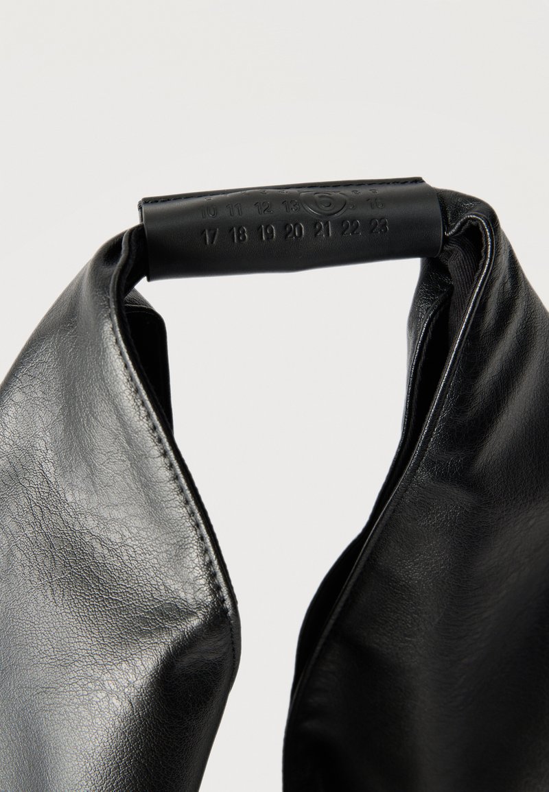 Sac à main en cuir noir avec poignée rembourrée, présentant des numéros en relief de 10 à 23 et des détails en couture sur un fond uni.