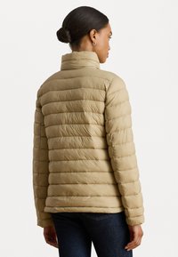 Giacca puffer beige con design trapuntato orizzontale, colletto alto e texture liscia. Ha maniche aderenti e arriva in vita.