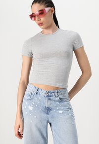 Camiseta gris ajustada combinada con jeans de denim desgastados en un tono azul claro con parches. Los accesorios incluyen gafas de sol con un tinte rosa.